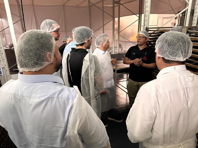 Foto mostra de blusa preta e touca branca fazendo uma explicação a outros homens também com toucas