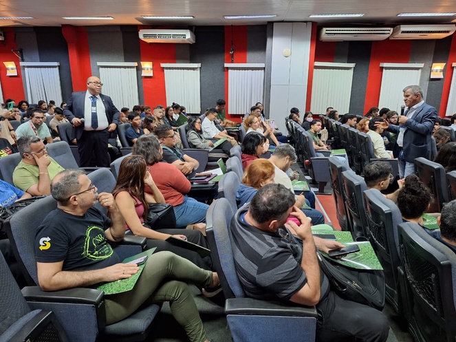 Foto mostra homem em pé falando a várias pessoas