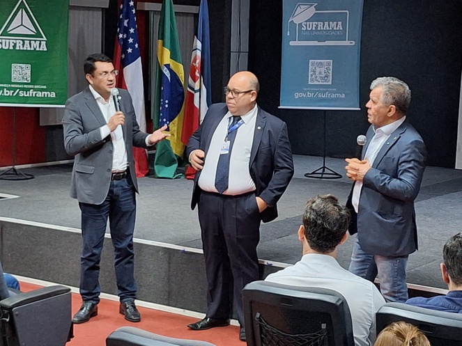 Foto mostra três homens em pé e de paletó em evento público