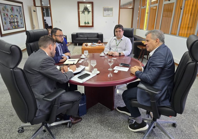 Foto mostra quatro homens sentados à mesa numa reunião