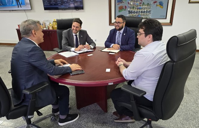 Foto mostra quatro homens sentados à mesa durante uma reunião