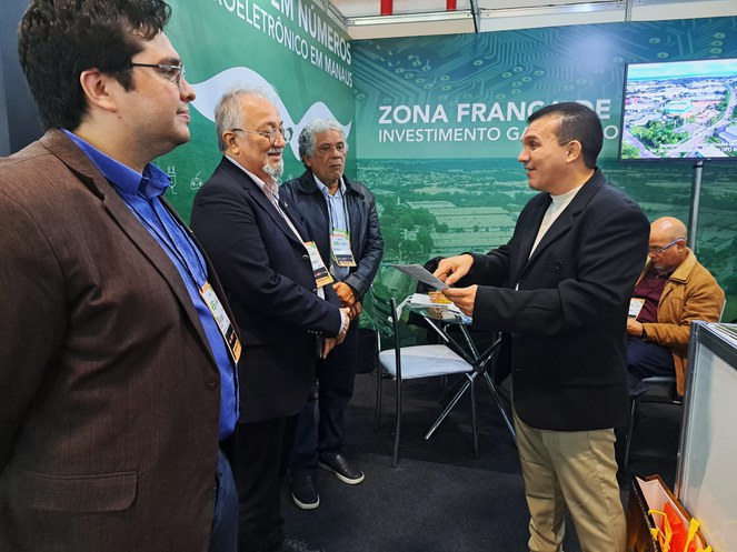 Foto mostra um homem de paletó apontando para um folder e fazendo uma explanação a um grupo de outros três homens