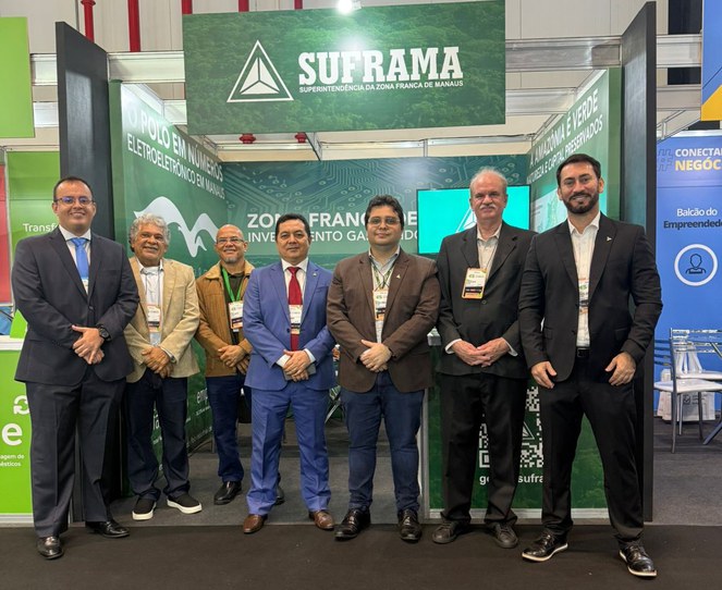 Foto mostra grupo de homens posando para foto em frente a um estande com o nome Suframa