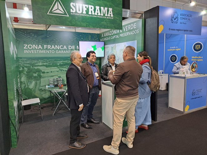 Foto mostra homens atendendo outro homem em um estande armado numa feira de eletroeletrônicos