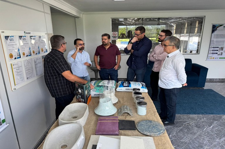 Imagem mostra seis homens ao redor de uma mesa contendo produtos da empresa expostos, como argamassa, entre outros