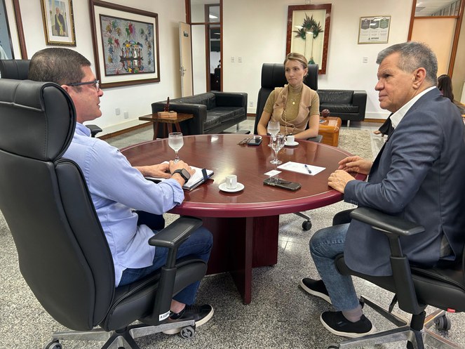 Foto mostra um homem de blusa azul fazendo uma explicação a outro homem de blazer, observados por uma mulher