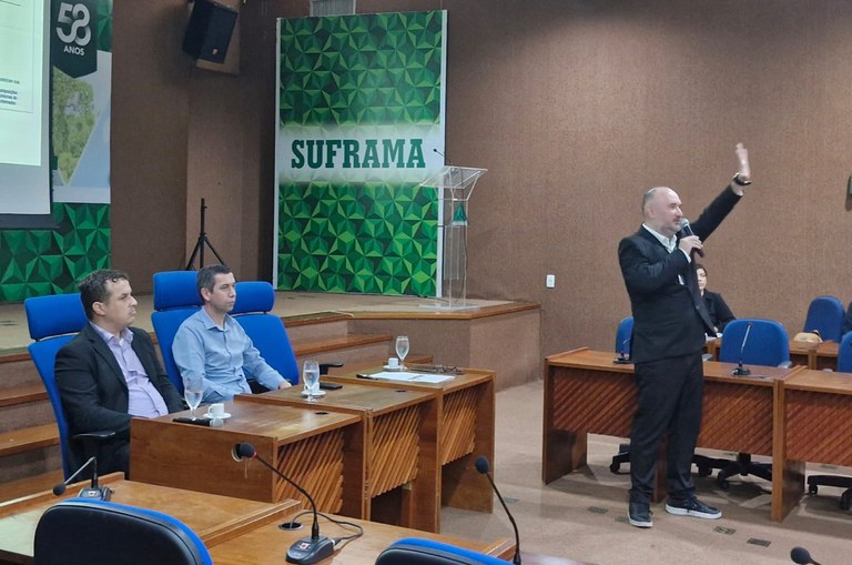 Foto mostra homem com microfone na mão direita, de blazer e calça escuros erguendo o braço, e erguendo o braço esquerdo 