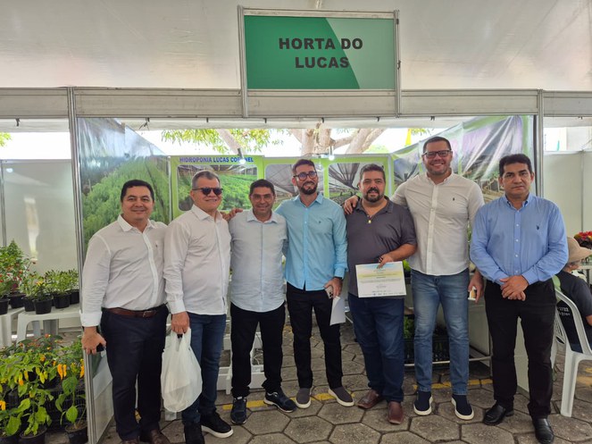 Foto mostra homens em frente a um estande, com um deles segurando um certificado