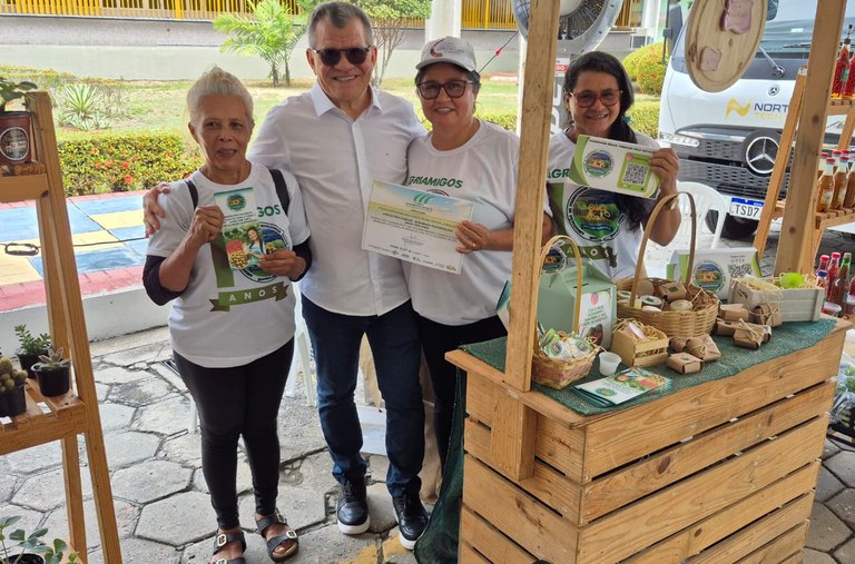 Foto mostra homens em frente a um estande, com um deles segurando um certificado