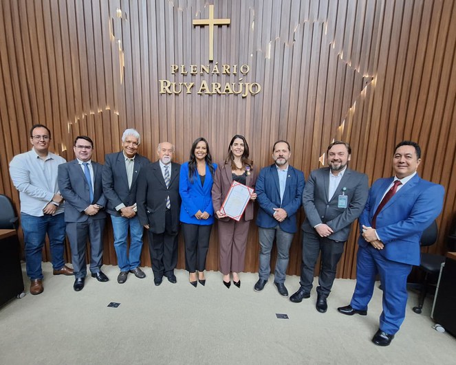 Foto mostra mulher segurando documento ao lado de um grupo de pessoas