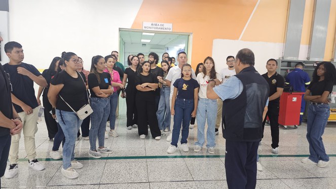 Foto mostra homem de azul dando uma explicação a grupo de pessoas em uma fábrica