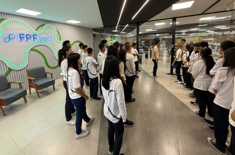 Foto mostra grupo de alunos de blusa branca conversando com dois homens de blusa bege