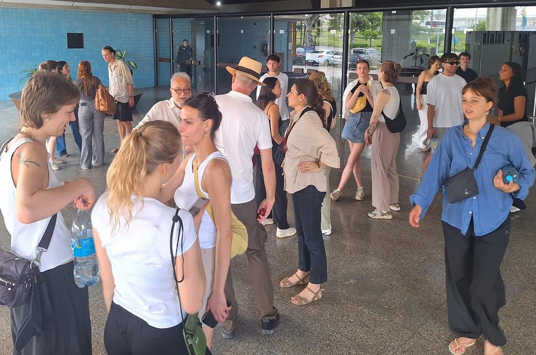 Foto mostra grupo de pessoas conversando, com destaque para uma mulher de blusa azul à direita da foto