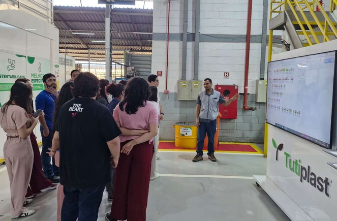 Foto mostra homem fazendo explanação para grupo de pessoas com o apoio de um painel