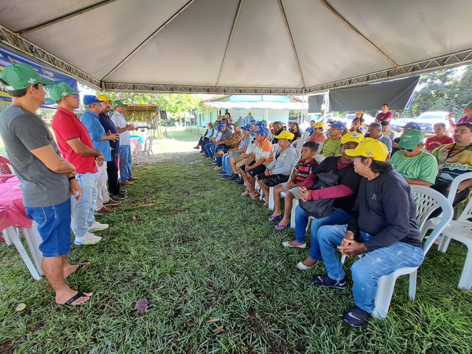 Foto mostra um grupo de pessoas em pé em um evento prestigiado por outro grupo de pessoas sentadas