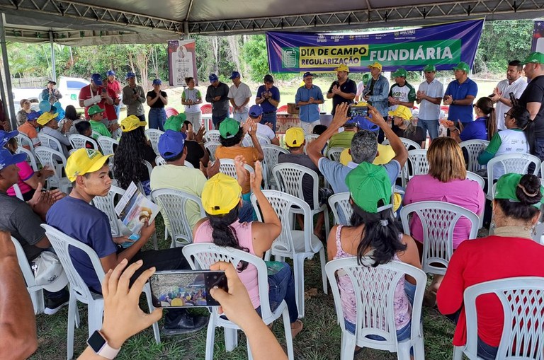 Foto mostra grupo de pessoas em pé em um evento prestigiado por outro grupo de pessoas sentadas