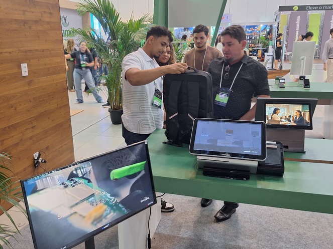 Foto mostra pessoas olhando para bolsa preta e notebooks