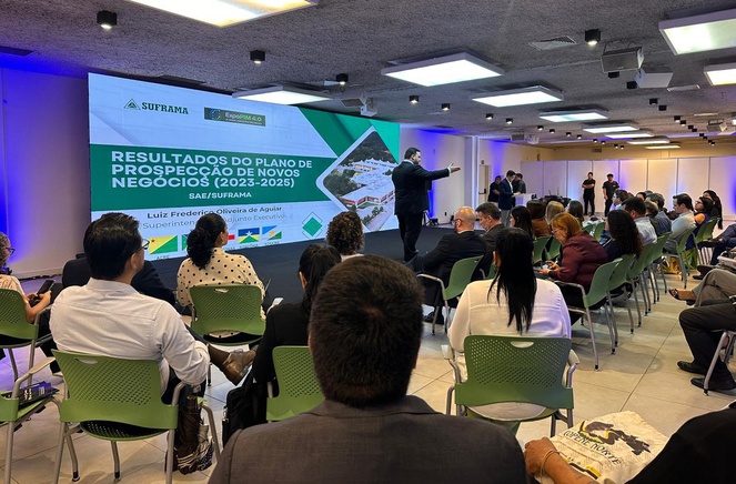 Foto mostra um homem de paletó e grava falando em público com um telão como apoio