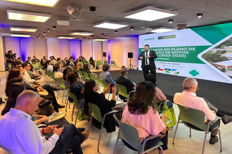 Foto mostra homem de paletó e grava falando em público com um telão como apoio