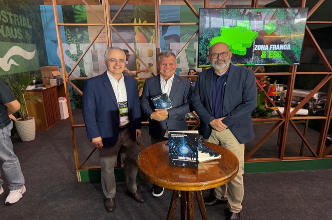 Foto mostra homem segurando livro ao lado de outros dois homens