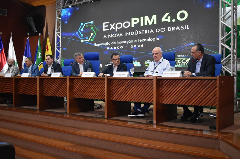 Sete autoridades masculinas estão sentadas à mesa em auditório durante o lançamento da ExpoPIM 4.0, com painel ao fundo exibindo o tema “A nova indústria do Brasil”