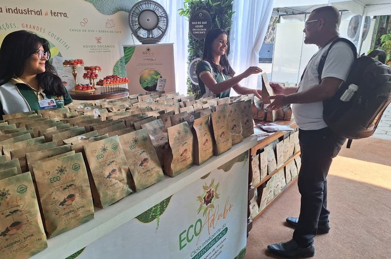 Foto mostra mulher entregando sacola a homem observada por outra mulher