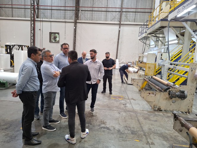 Foto mostra homens reunidos numa fábrica de produtos plásticos