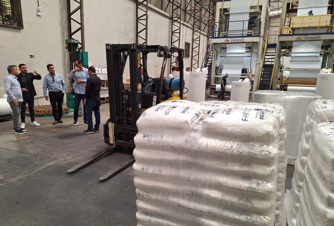 Foto mostra homens reunidos numa fábrica de produtos plásticos