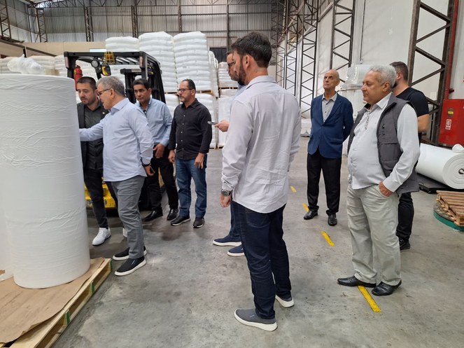 Foto mostra homem de blusa branca e óculos escuros apontando para um produto plástico