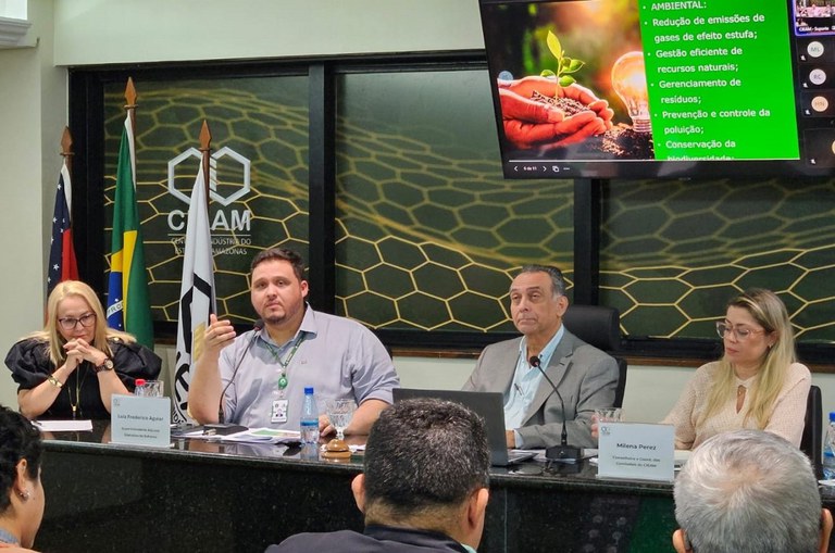 Foto mostra homem vestido de blusa lilás clara e se pronunciando durante evento