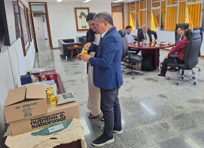 Foto mostra o superintendente da Autarquia (de terno azul marinho e se pronunciando) apresentando produtos amazônicos a representante do INPI