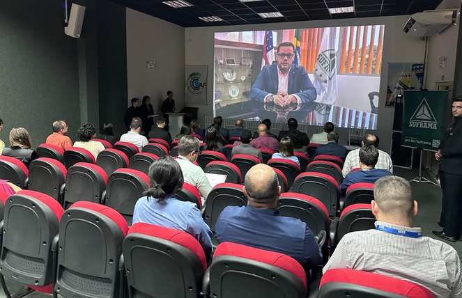 Foto mostra homem falando em um telão para um auditório lotado