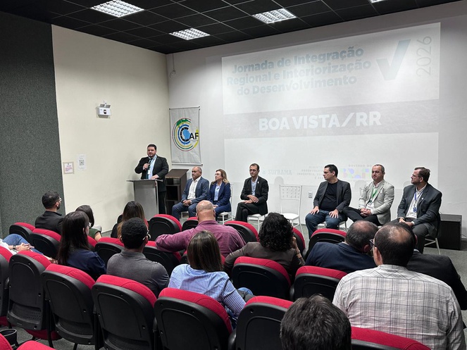 Foto mostra um homem falando em um auditório lotado com telão ao fundo