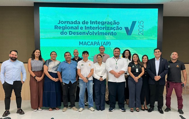 Foto mostra grupo de pessoas posando para foto com um painel ao fundo