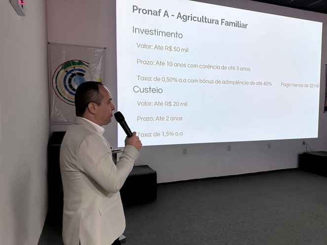 Foto mostra homem de blazer falando ao microfone com o apoio de um telão