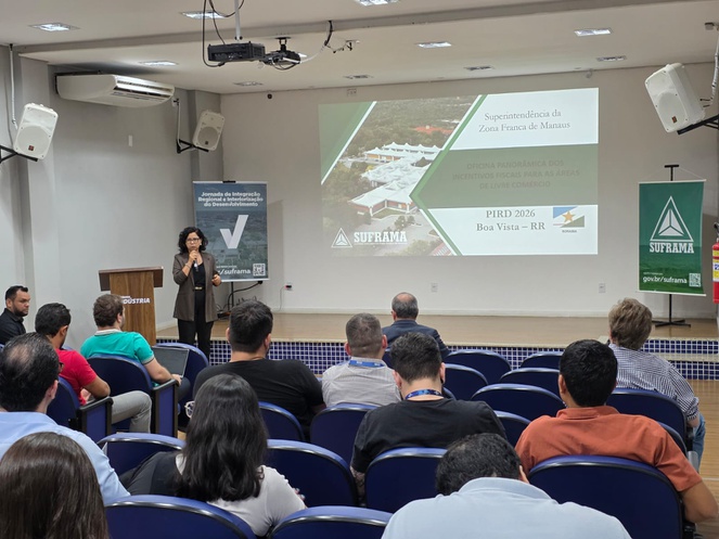 Foto mostra mulher falando ao microfone com telão ao fundo