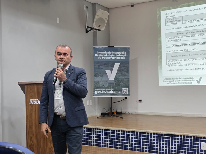 Foto mostra homem falando ao microfone e um telão
