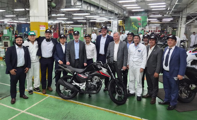 Foto mostra pessoas posando para foto em uma fábrica de motocicletas