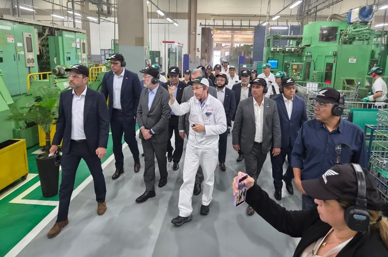 Foto mostra homem de uniforme branco mostrando fábrica a visitantes