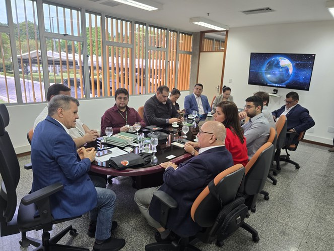 Foto mostra homem de blazer azul em conversa com homem de óculos durante uma reunião