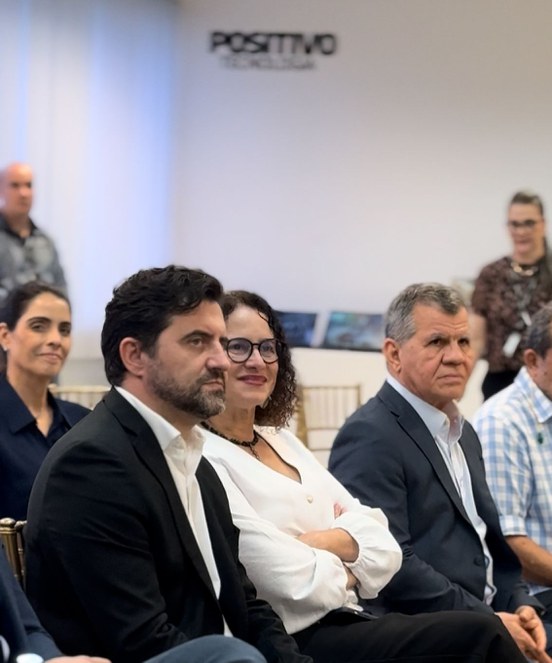 Foto mostra mulher de blusa branca entre dois homens