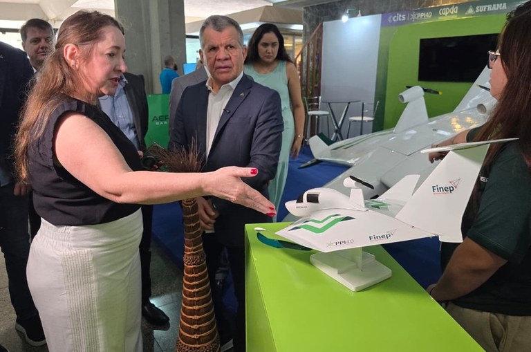 Foto mostra mulher mostrando uma maquete de aeronave a um homem de blazer 