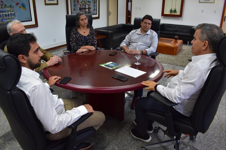 Foto mostra homem de blusa branca e calça preta conversando com outros três homens e uma mulher