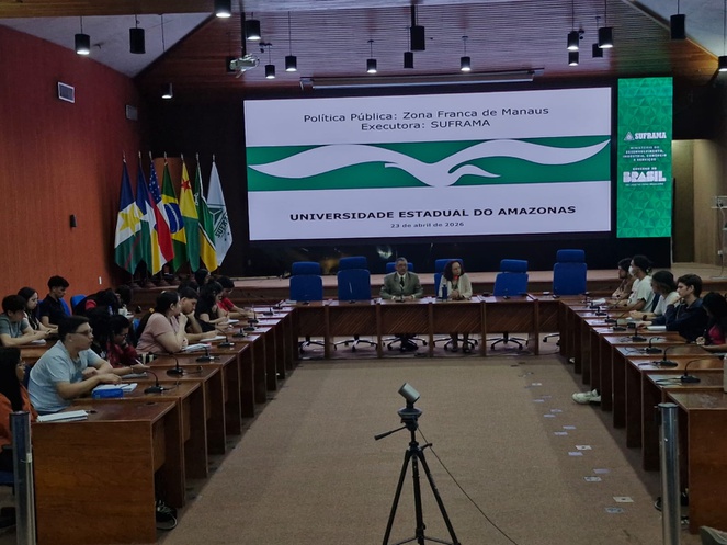 Foto mostra pessoas reunidas para uma palestra, com o apoio de um telão
