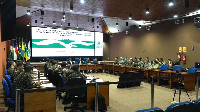 Foto mostra grupo de pessoas numa reunião, com um telão de apoio