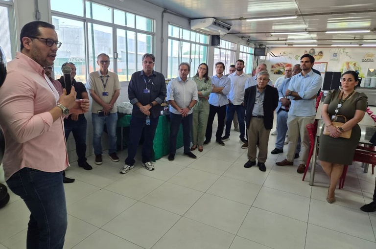 Foto mostra homem falando ao microfone para um pequeno grupo de pessoas