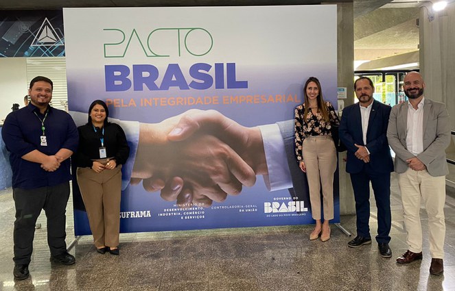 Foto mostra quatro pessoas posando para sessão de foto em frente a uma placa grande