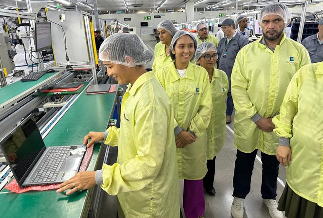 Foto mostra mulher mexendo num notebook observada por outras pessoas