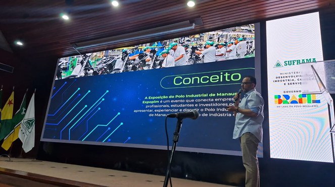 Foto mostra homem fazendo uma apresentação com um telão como apoio