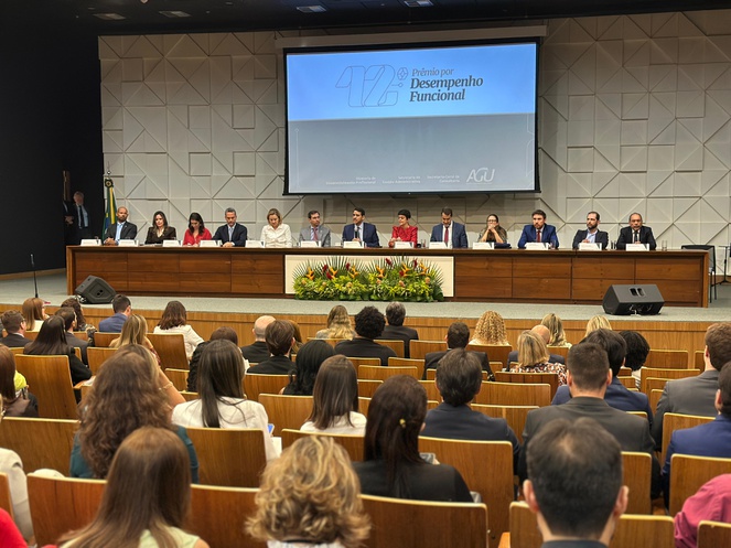 Foto mostra pessoas num evento e com um telão ao fundo
